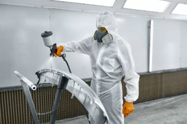 Technician in safety clothing spraying car paint